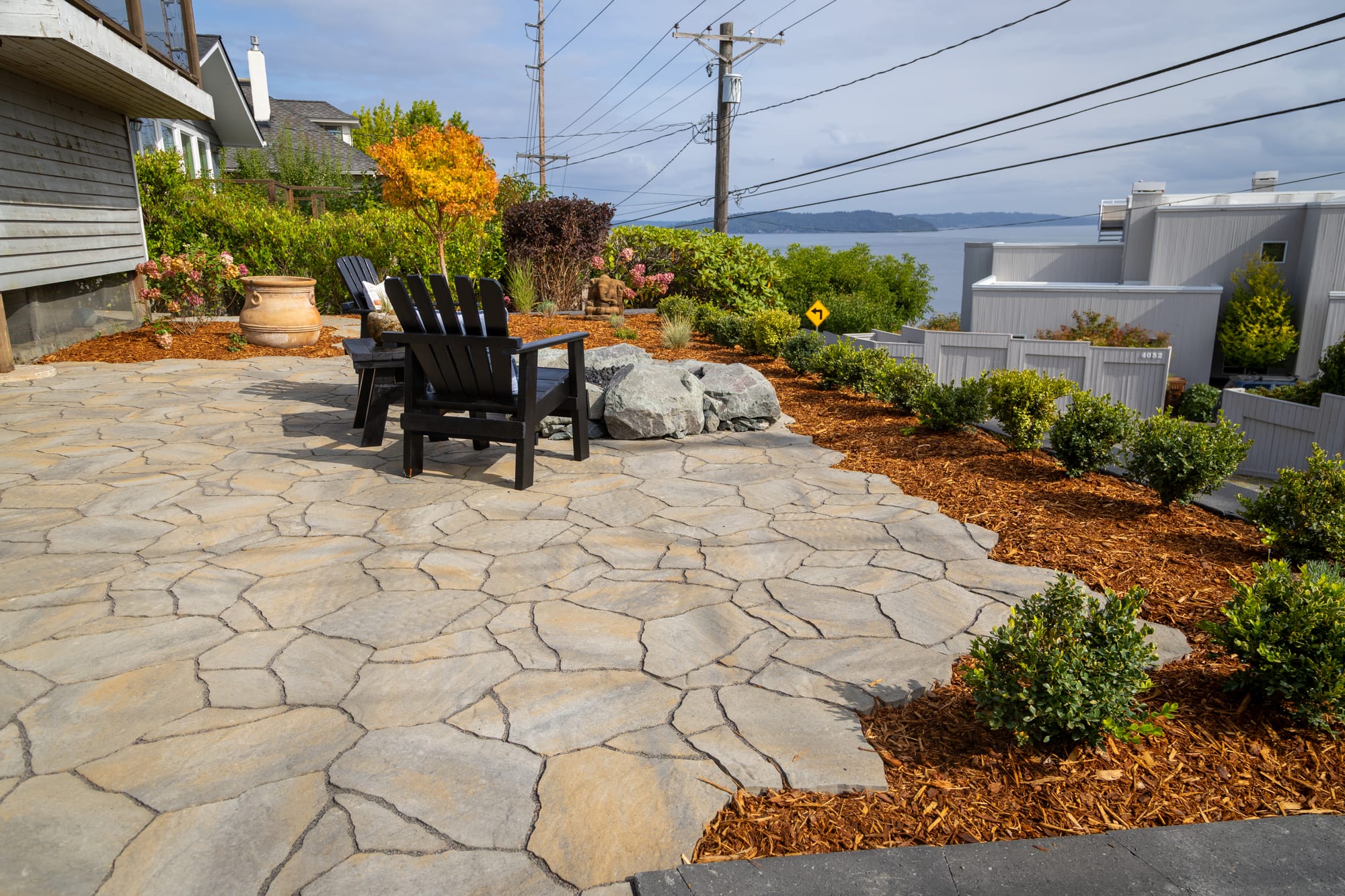 The edge of the paver patio with curving planting beds of low rounded shrubs in bark mulch