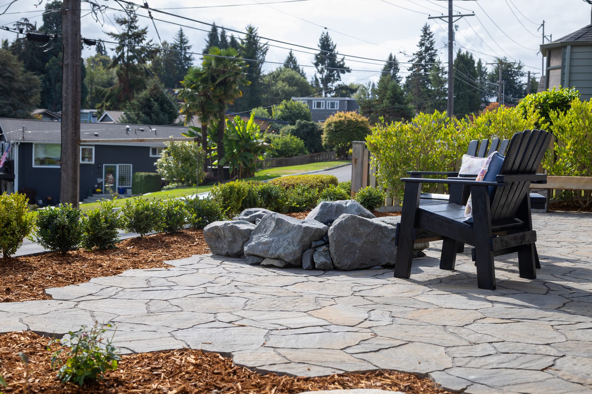 The patio looking toward the street and neighborhood, with boulders around the fire pit and a hedge along the edge